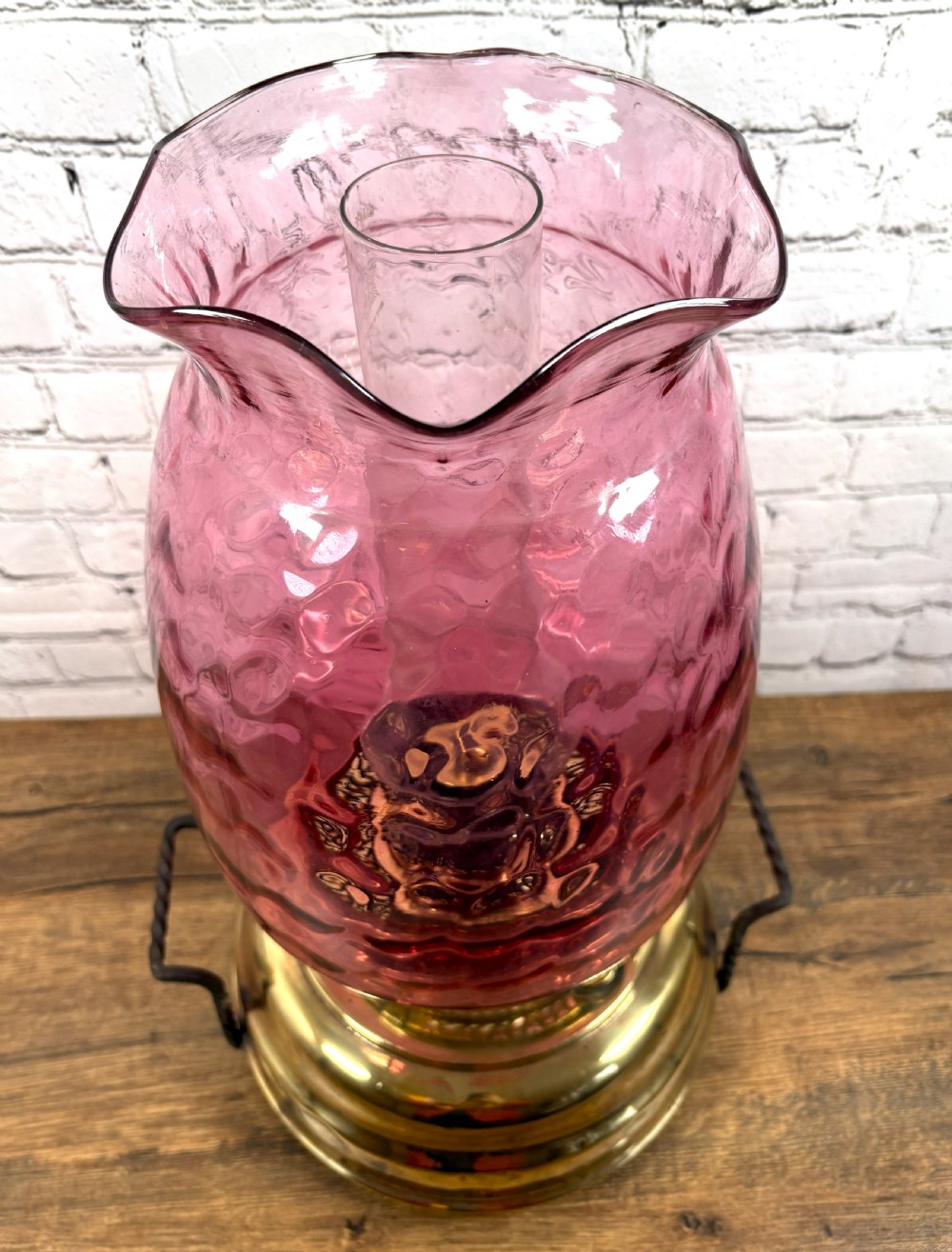 An antique Victorian oil lamp featuring a stepped polished brass base with twin wrought iron handles and a large dimpled cranberry glass hurricane shade. View III