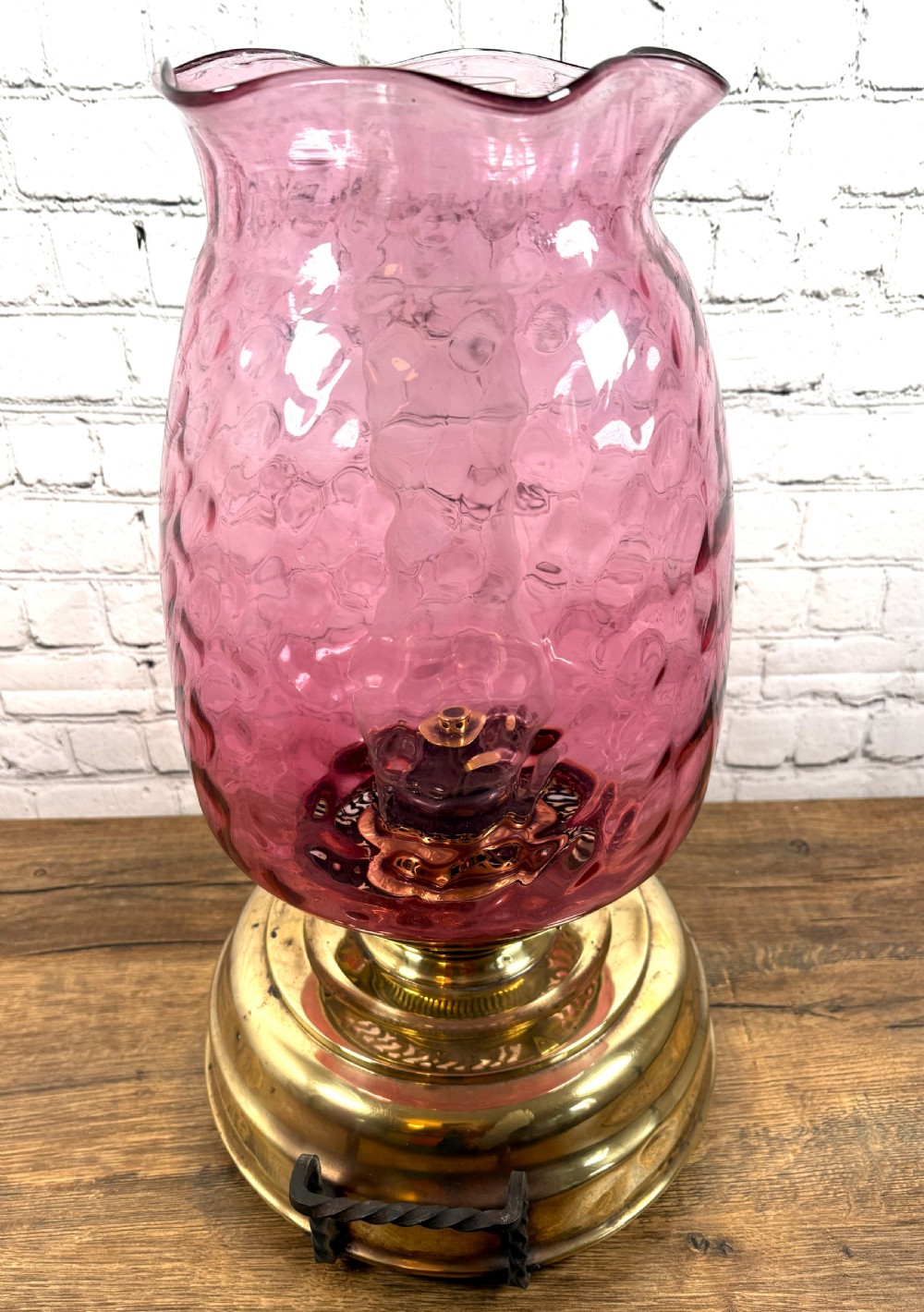 An antique Victorian oil lamp featuring a stepped polished brass base with twin wrought iron handles and a large dimpled cranberry glass hurricane shade. View IV