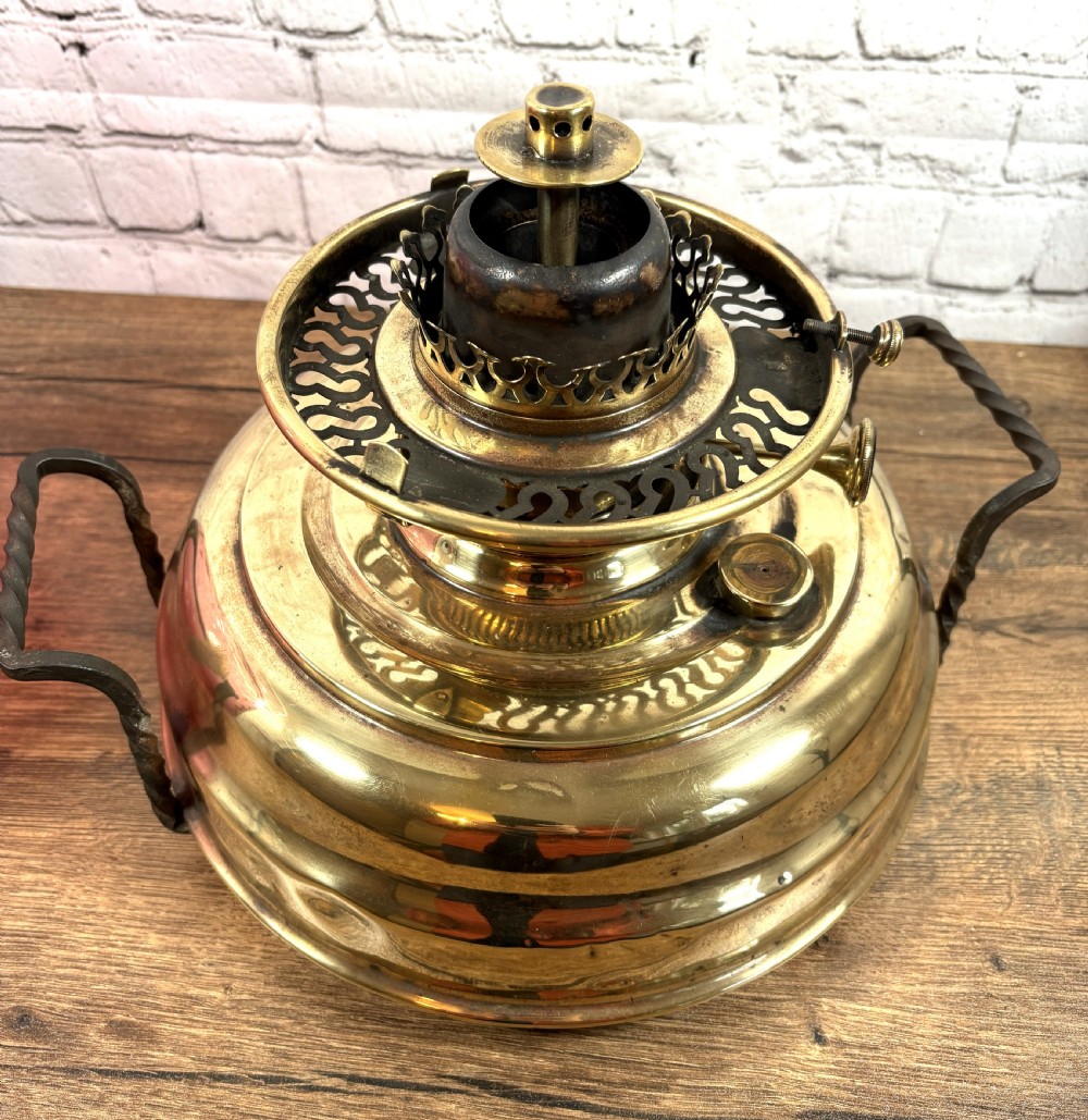 An antique Victorian oil lamp featuring a stepped polished brass base with twin wrought iron handles and a large dimpled cranberry glass hurricane shade. View V