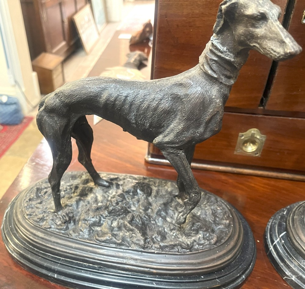 A pair of patinated dark bronze whippet dog sculptures standing on molded oval black marble bases. View II