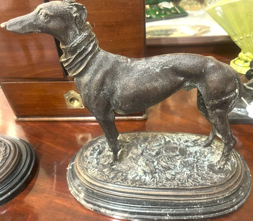 A pair of patinated dark bronze whippet dog sculptures standing on molded oval black marble bases. View V