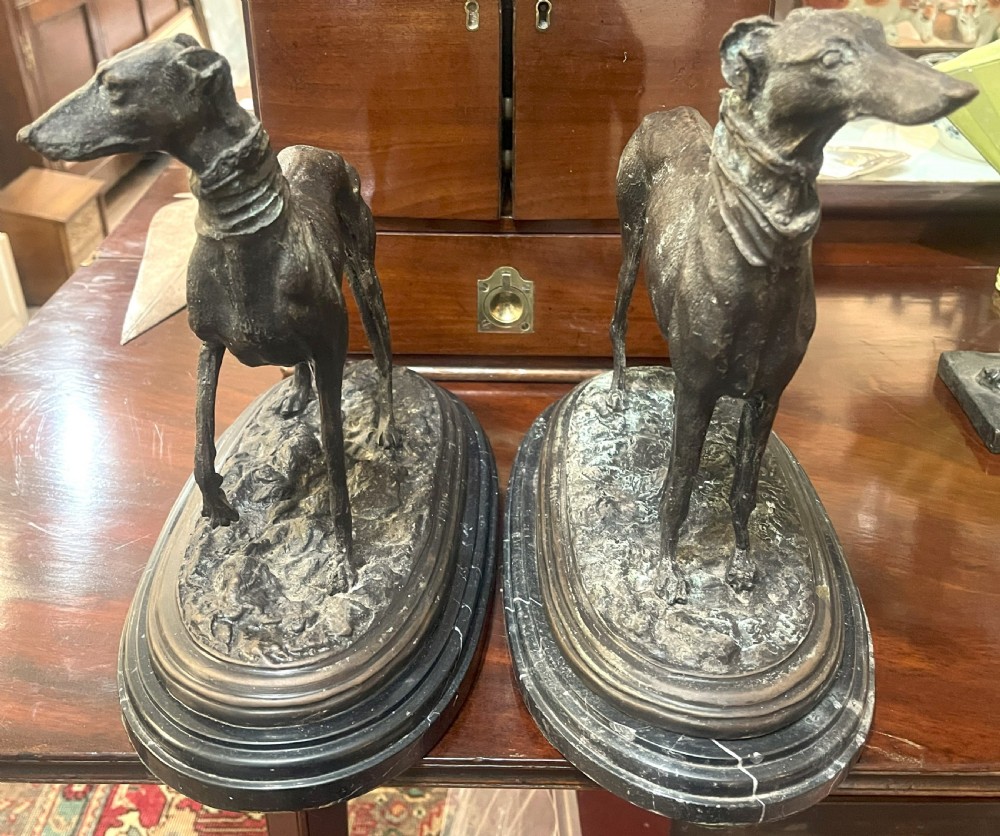 A pair of patinated dark bronze whippet dog sculptures standing on molded oval black marble bases. View VIII