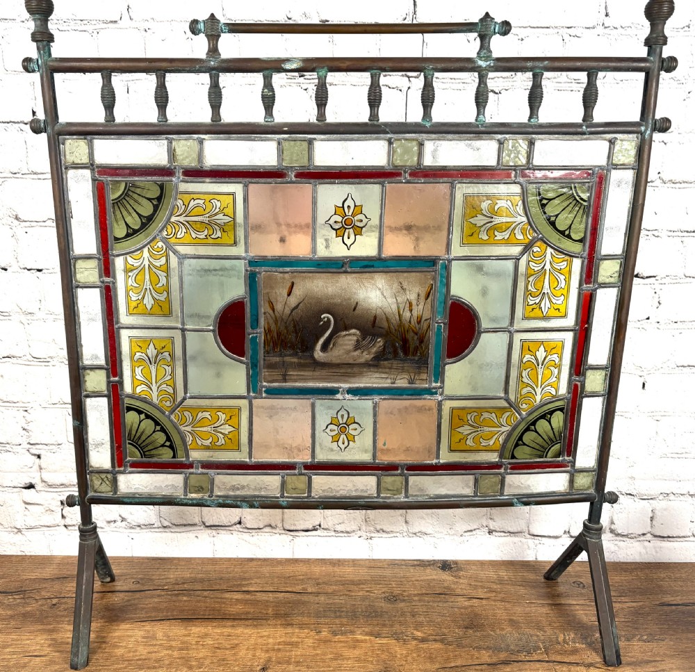 Victorian brass-framed fireguard featuring leaded stained glass panels in yellow, red, and clear geometric patterns surrounding a central hand-painted panel of a swan.