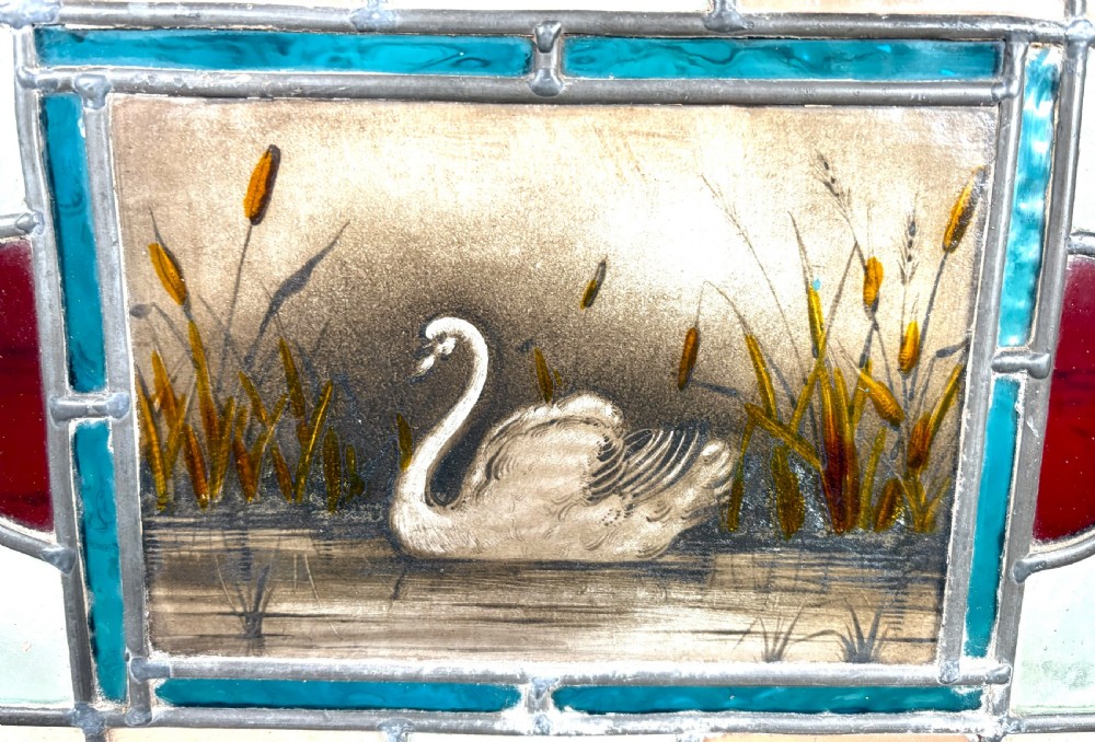 Victorian brass-framed fireguard featuring leaded stained glass panels in yellow, red, and clear geometric patterns surrounding a central hand-painted panel of a swan. View III