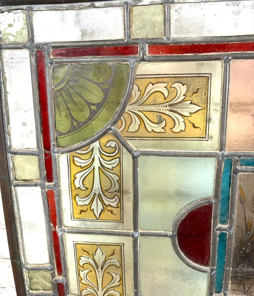 Victorian brass-framed fireguard featuring leaded stained glass panels in yellow, red, and clear geometric patterns surrounding a central hand-painted panel of a swan. View VI