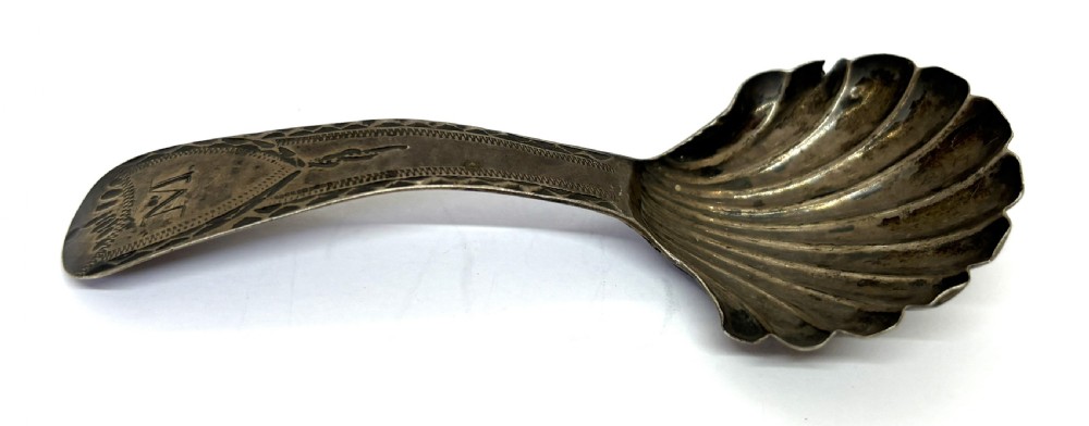 A late eighteenth-century sterling silver caddy spoon featuring a fluted shell bowl and a curved handle decorated with bright-cut engraving.