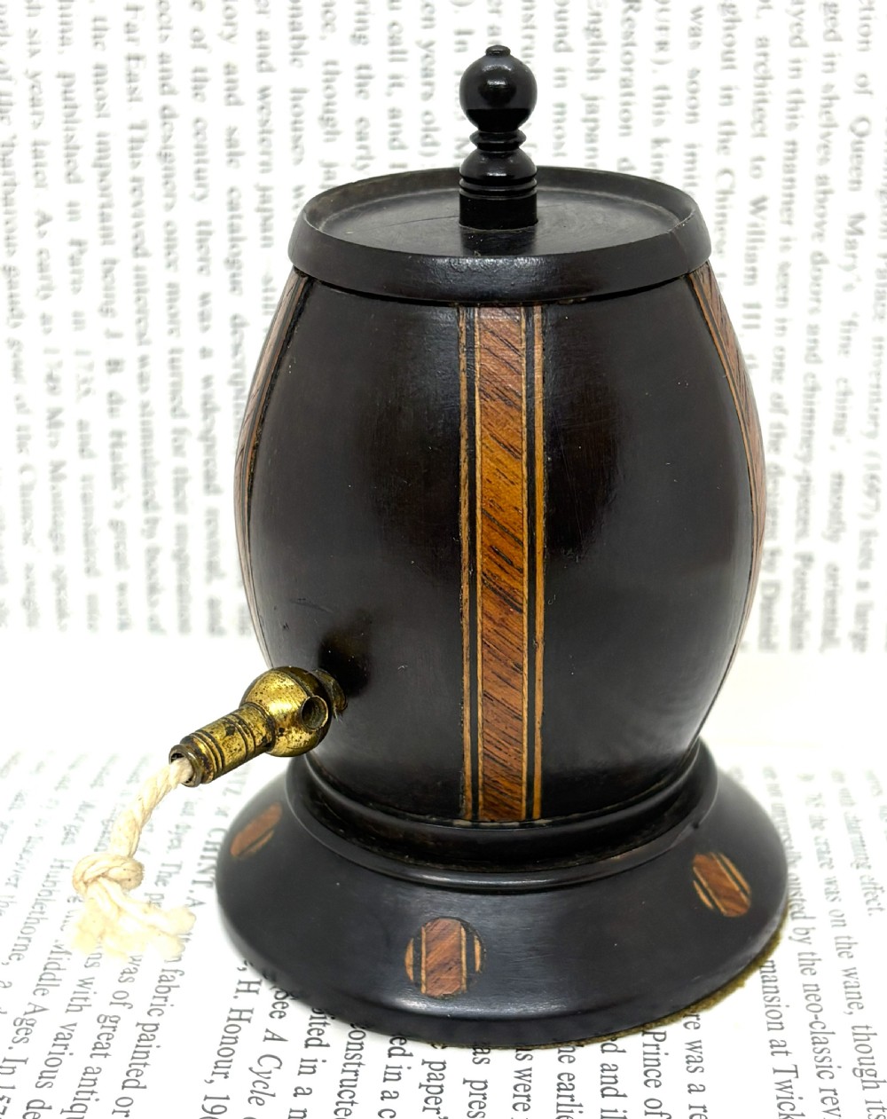 A turned dark lignum vitae wooden string barrel featuring inlaid geometric wood bands, a top turned finial, and a brass dispensing nozzle.