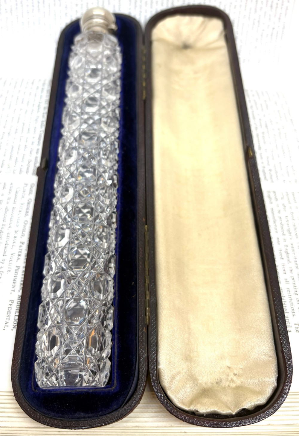 An elongated Victorian cut glass scent bottle with a silver cap resting inside an open velvet and silk lined presentation case.