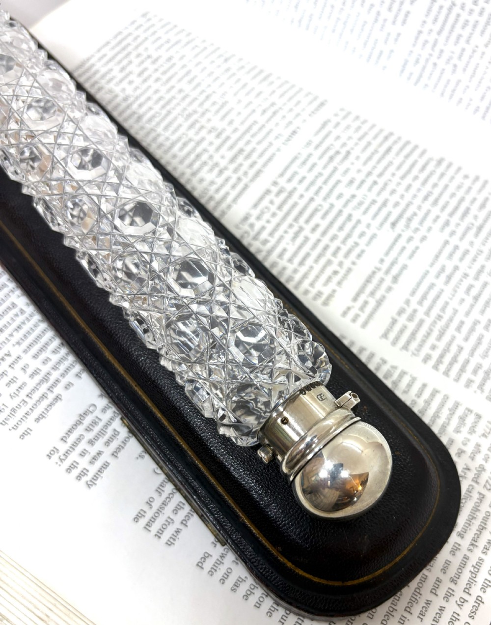 An elongated Victorian cut glass scent bottle with a silver cap resting inside an open velvet and silk lined presentation case. View IV