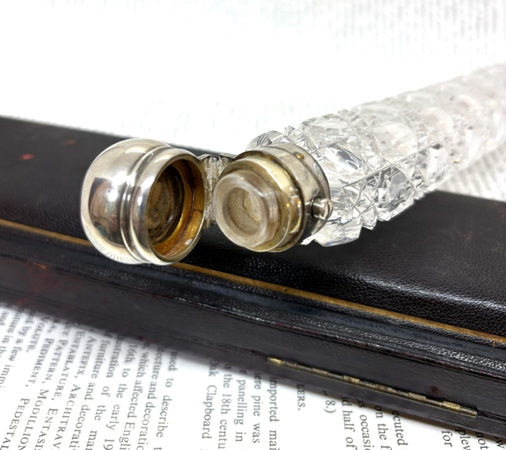 An elongated Victorian cut glass scent bottle with a silver cap resting inside an open velvet and silk lined presentation case. View V