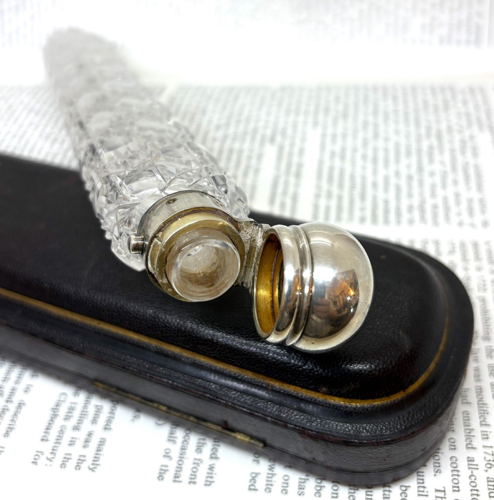 An elongated Victorian cut glass scent bottle with a silver cap resting inside an open velvet and silk lined presentation case. View VI