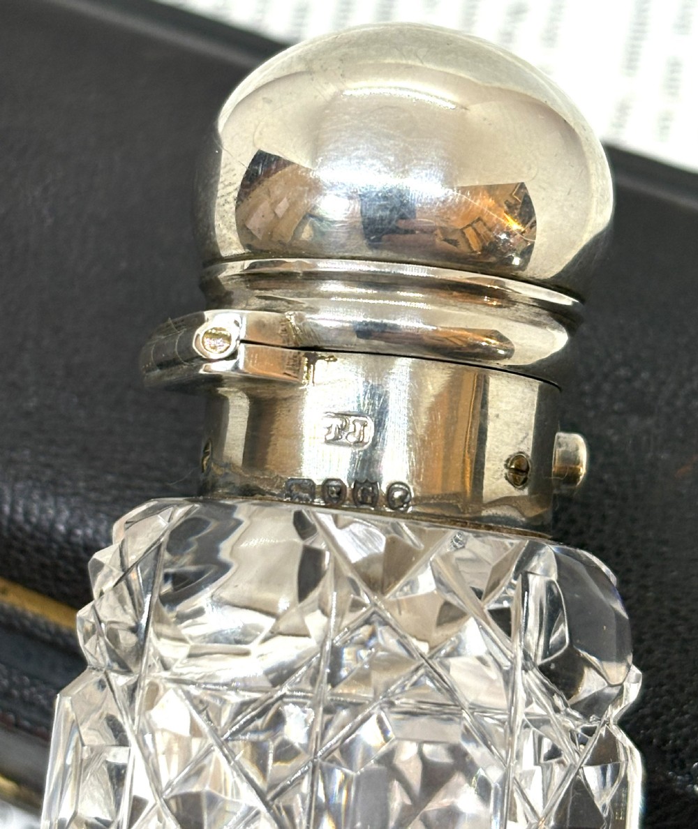 An elongated Victorian cut glass scent bottle with a silver cap resting inside an open velvet and silk lined presentation case. View VII