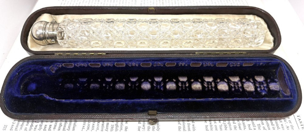 An elongated Victorian cut glass scent bottle with a silver cap resting inside an open velvet and silk lined presentation case. View IX