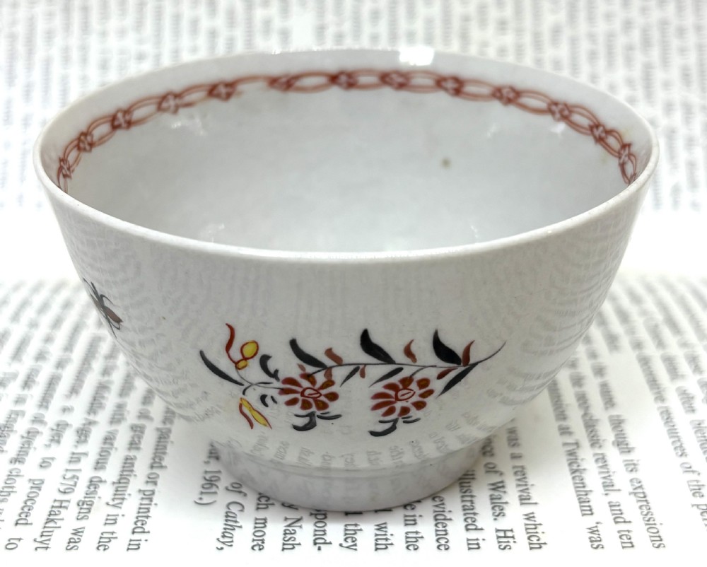 A Georgian Lowestoft white soft-paste porcelain tea bowl with hand-painted floral motifs and a reddish-brown internal chain border.