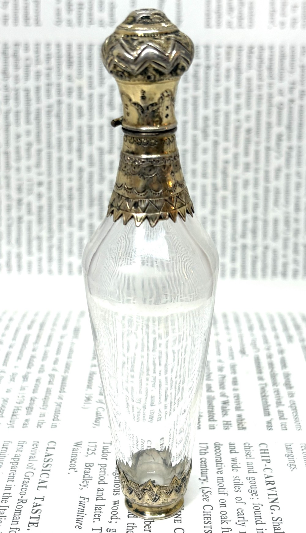 An early nineteenth-century clear fluted glass scent bottle with detailed silver-gilt engraved mounts on the top and base.