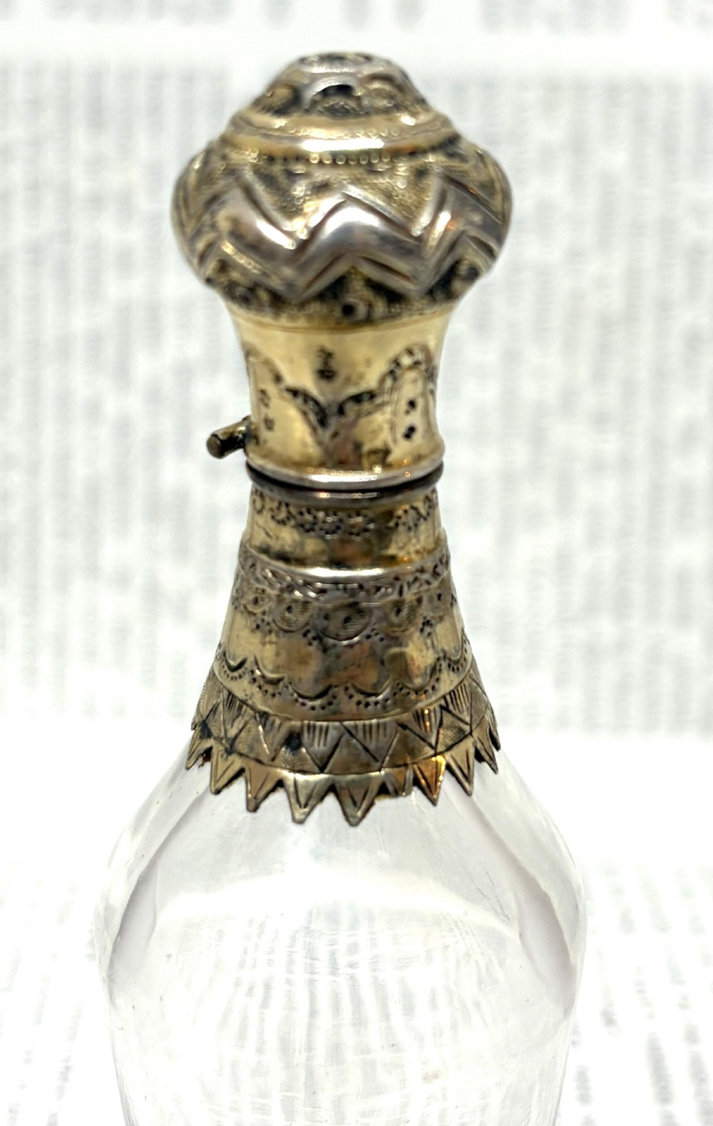 An early nineteenth-century clear fluted glass scent bottle with detailed silver-gilt engraved mounts on the top and base. View II