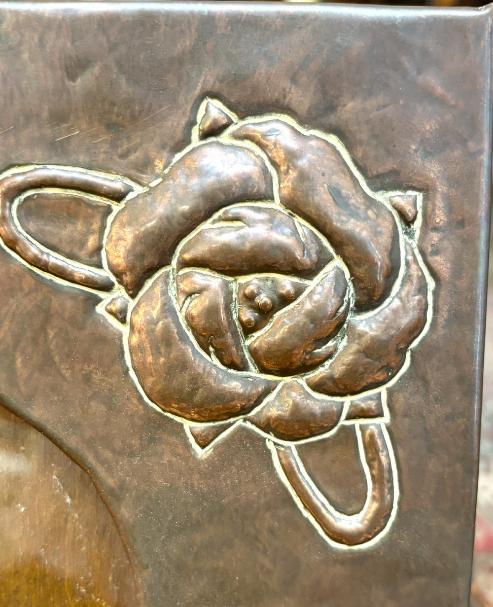 A hand-hammered rectangular copper picture frame featuring raised repousse rose motifs at each corner surrounding a central oval picture opening. View II