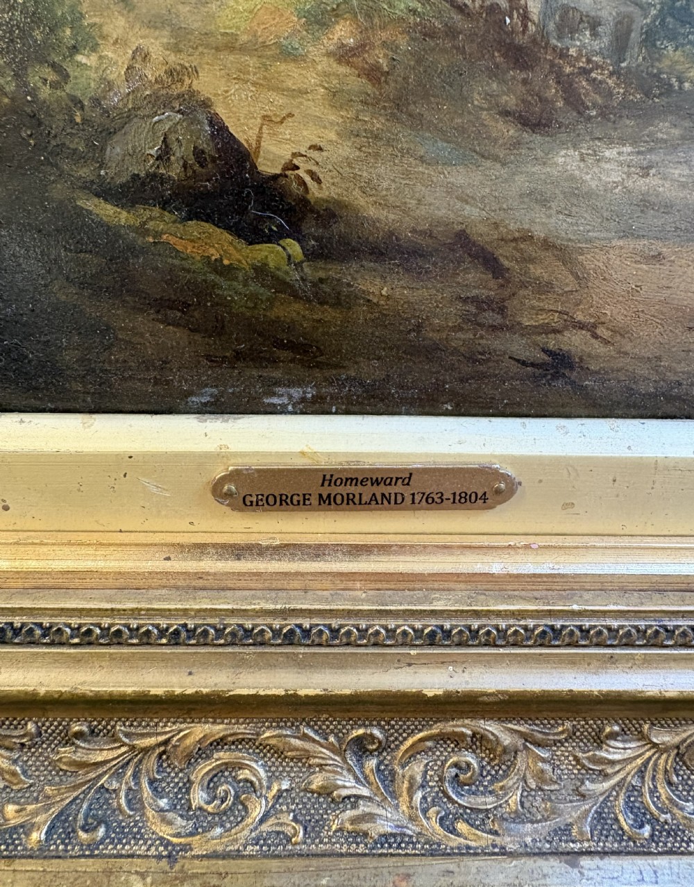 An antique oil painting on board depicting a rural figure walking near a cottage amidst trees and distant mountains, set within a carved gold gilt frame. View III