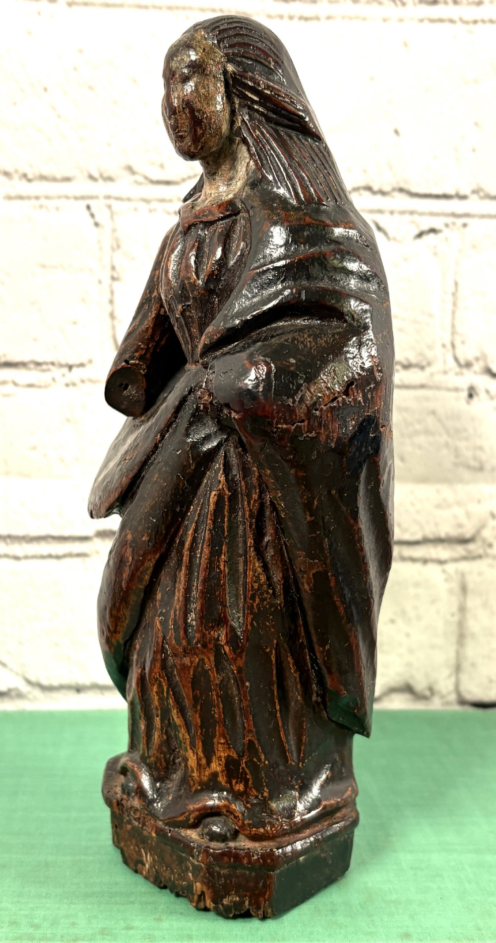 A 17th-century carved limewood figure of a female saint featuring draped robes, dark brown patina, and an octagonal base. View III