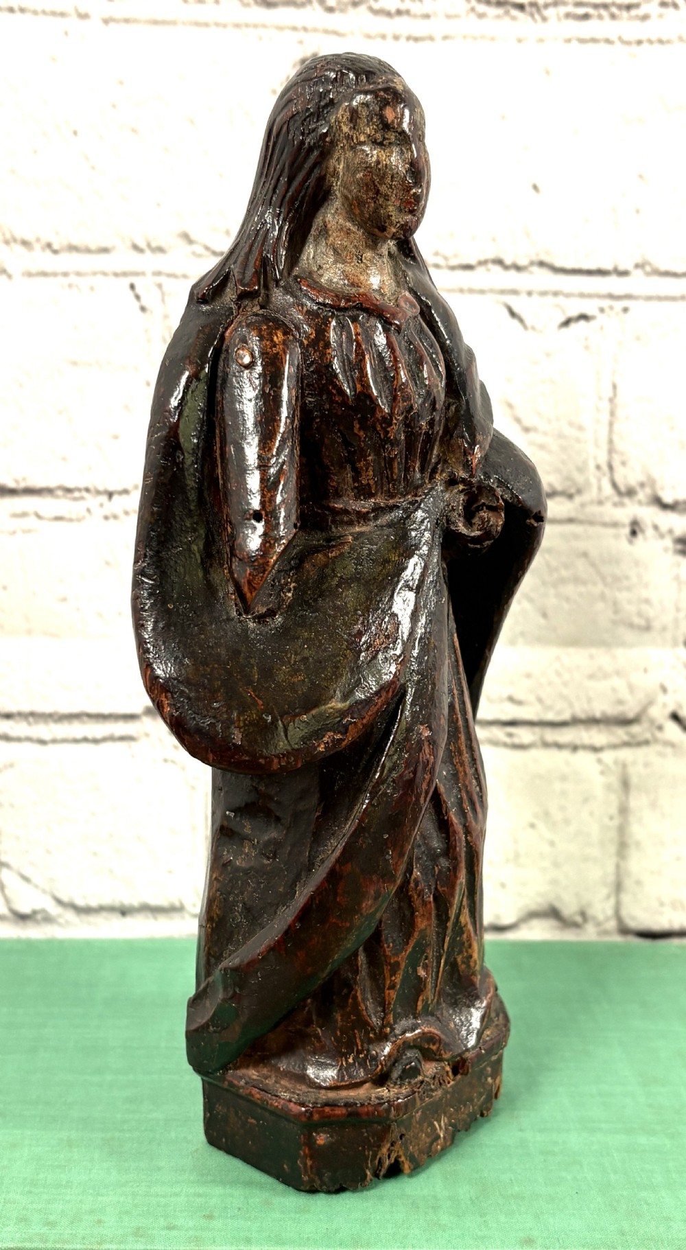 A 17th-century carved limewood figure of a female saint featuring draped robes, dark brown patina, and an octagonal base. View V