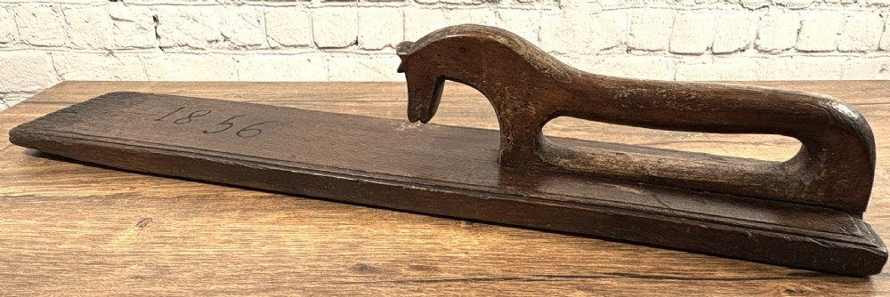 A dark carved wooden Norwegian mangle board featuring a handle shaped like a stylised horse and the carved date 1856.