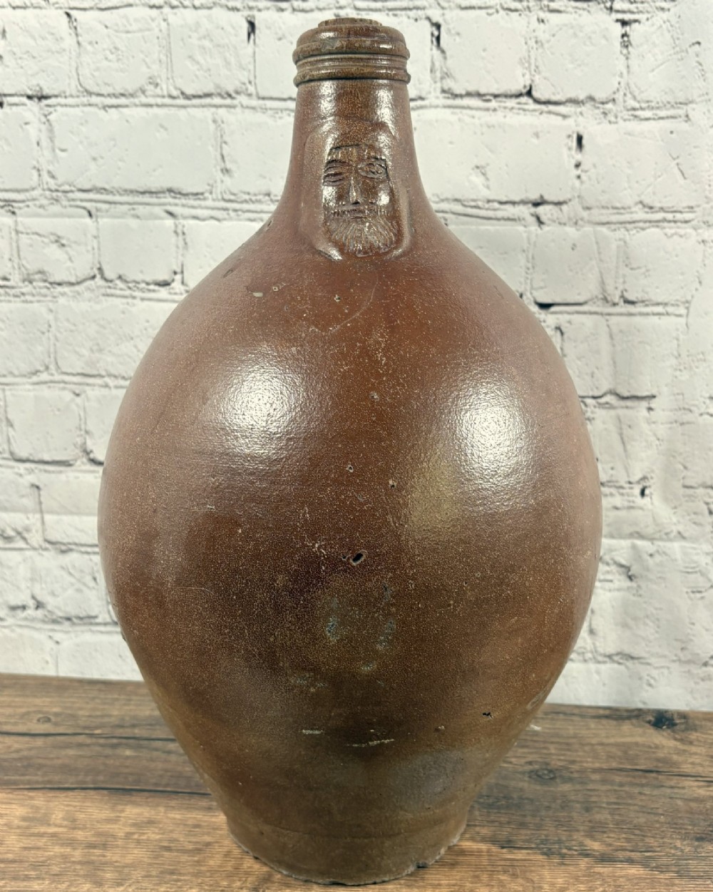 A large brown salt-glazed stoneware jug featuring a bulbous body and a relief mould of a bearded mask on the narrow neck.