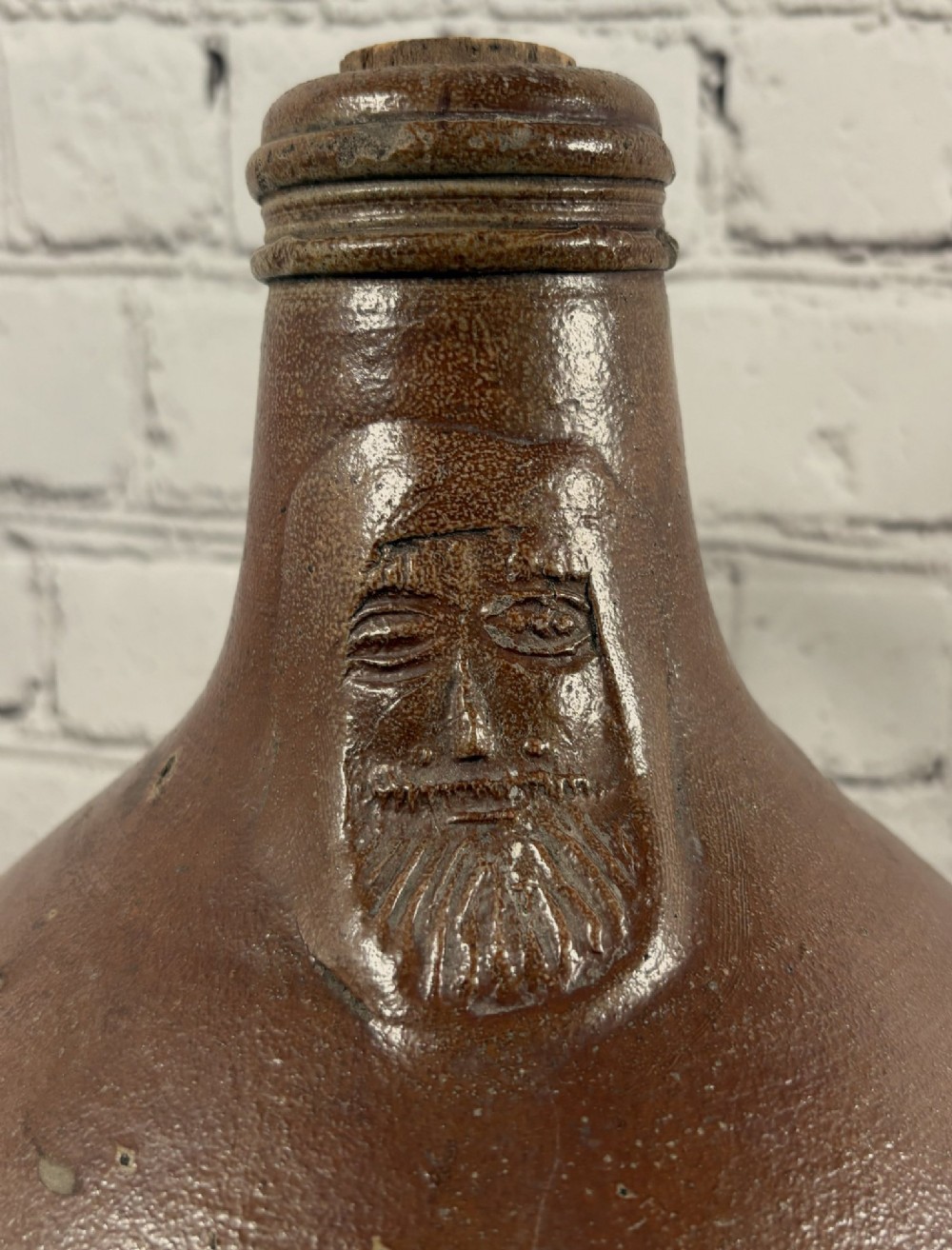 A large brown salt-glazed stoneware jug featuring a bulbous body and a relief mould of a bearded mask on the narrow neck. View II