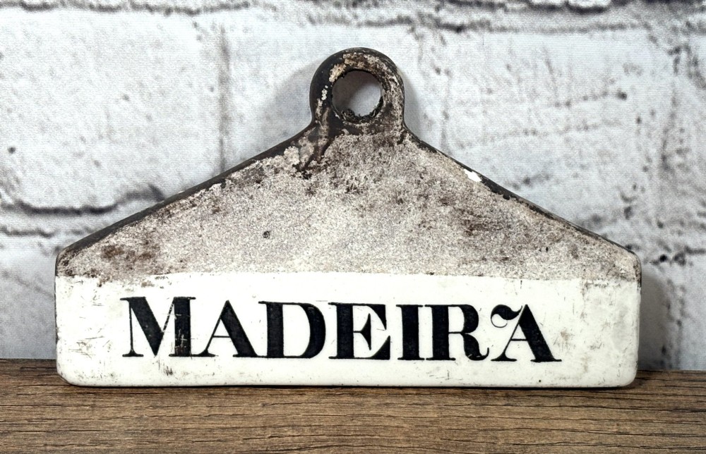 A 19th-century creamware pottery wine bin label featuring a triangular top aperture and black transfer-printed lettering spelling Madeira.