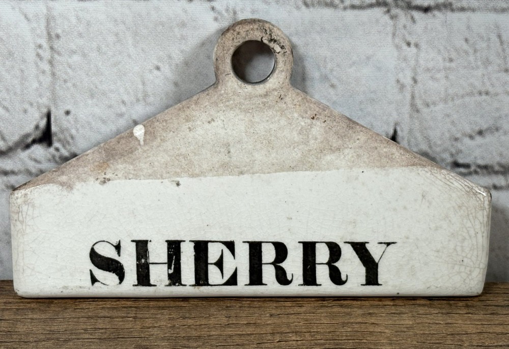 A 19th-century cream-glazed earthenware wine bin label featuring a top hanging hole and the word SHERRY printed in black serif lettering.