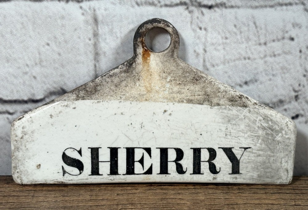 A 19th-century off-white glazed pottery wine bin label featuring the word SHERRY in black serif lettering with a top hanging hole.