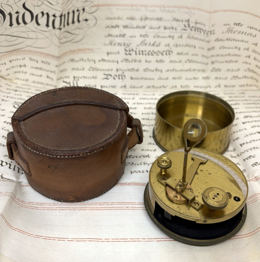 A 19th-century cylindrical brass surveying theodolite with an adjustable sight glass standing beside its original fitted brown leather carrying case. View II