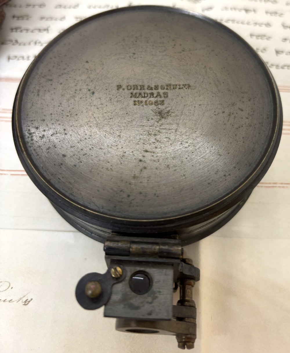 An early 20th-century blackened brass prismatic compass displayed open beside its original fitted brown leather carrying case. View V