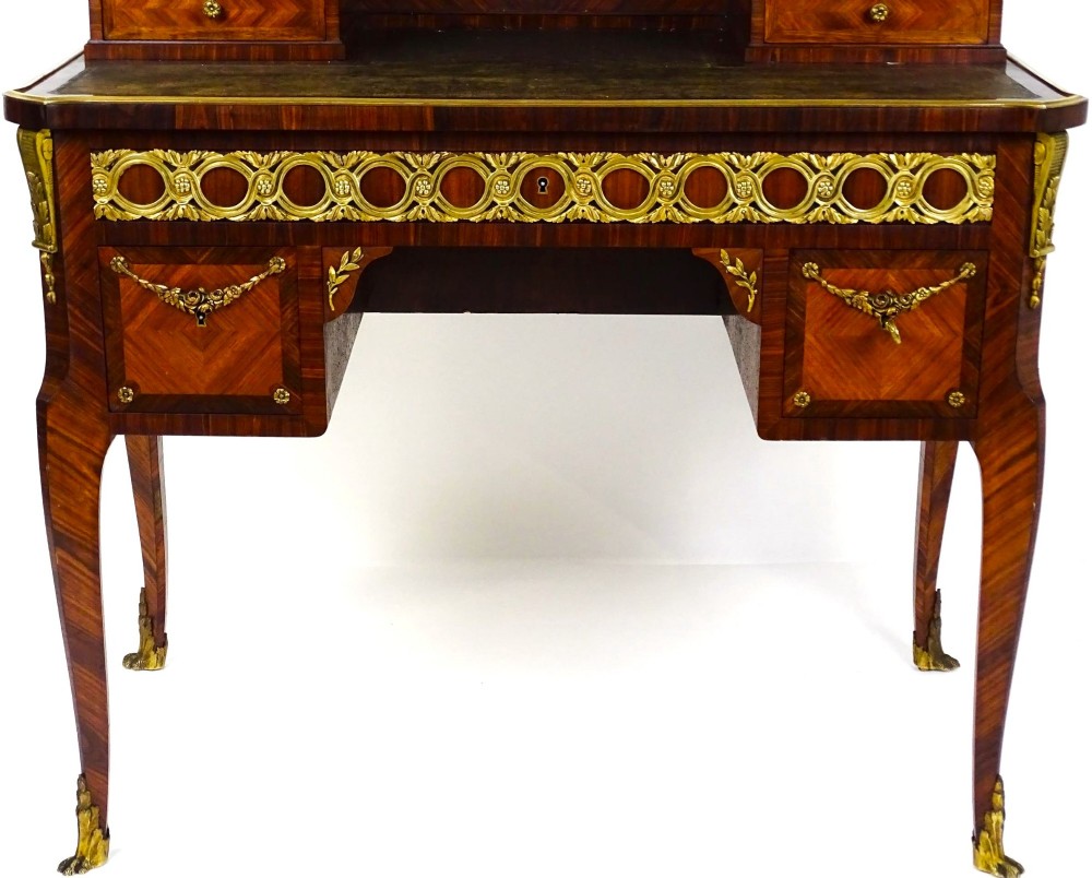 A French 19th-century kingwood writing desk with gilt-bronze ormolu mounts, upper pigeonholes and drawers, a central clock, and cabriole legs. View V