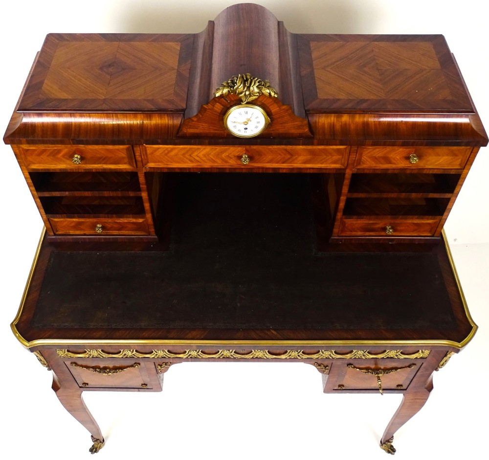 A French 19th-century kingwood writing desk with gilt-bronze ormolu mounts, upper pigeonholes and drawers, a central clock, and cabriole legs. View VII