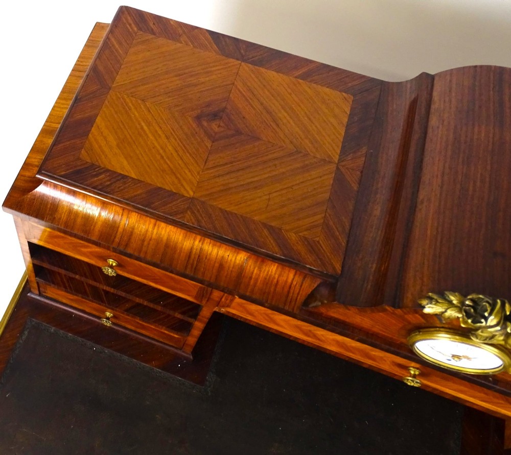 A French 19th-century kingwood writing desk with gilt-bronze ormolu mounts, upper pigeonholes and drawers, a central clock, and cabriole legs. View X