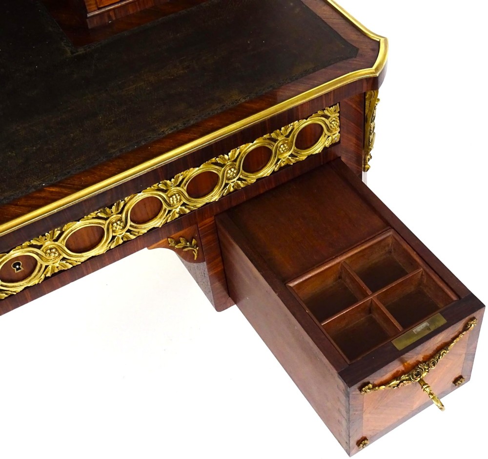 A French 19th-century kingwood writing desk with gilt-bronze ormolu mounts, upper pigeonholes and drawers, a central clock, and cabriole legs. View XI