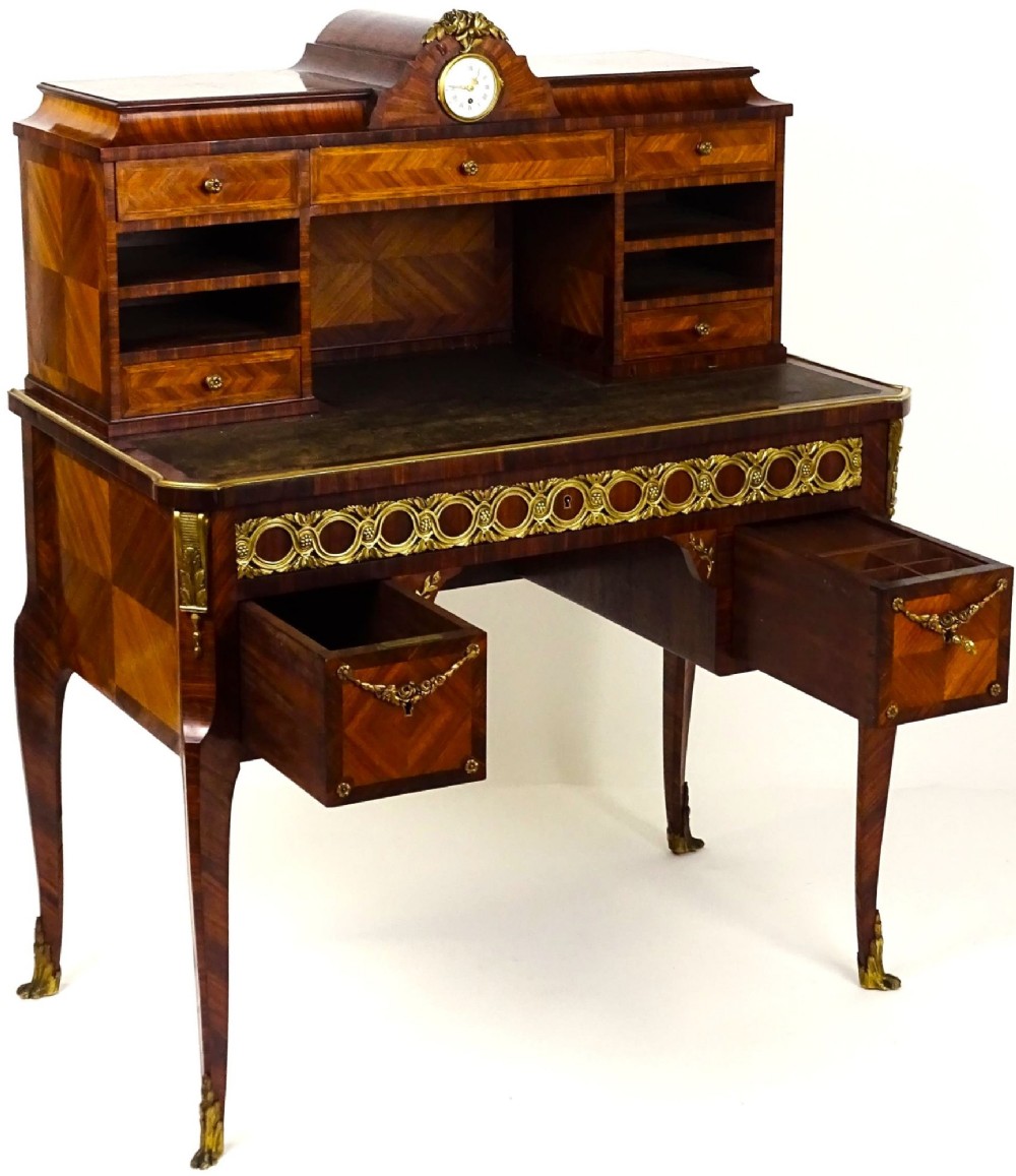 A French 19th-century kingwood writing desk with gilt-bronze ormolu mounts, upper pigeonholes and drawers, a central clock, and cabriole legs. View XIII