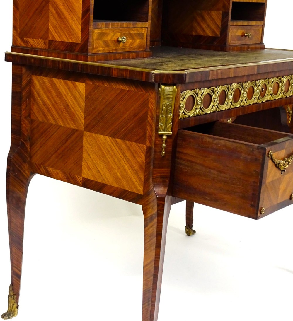 A French 19th-century kingwood writing desk with gilt-bronze ormolu mounts, upper pigeonholes and drawers, a central clock, and cabriole legs. View XIV