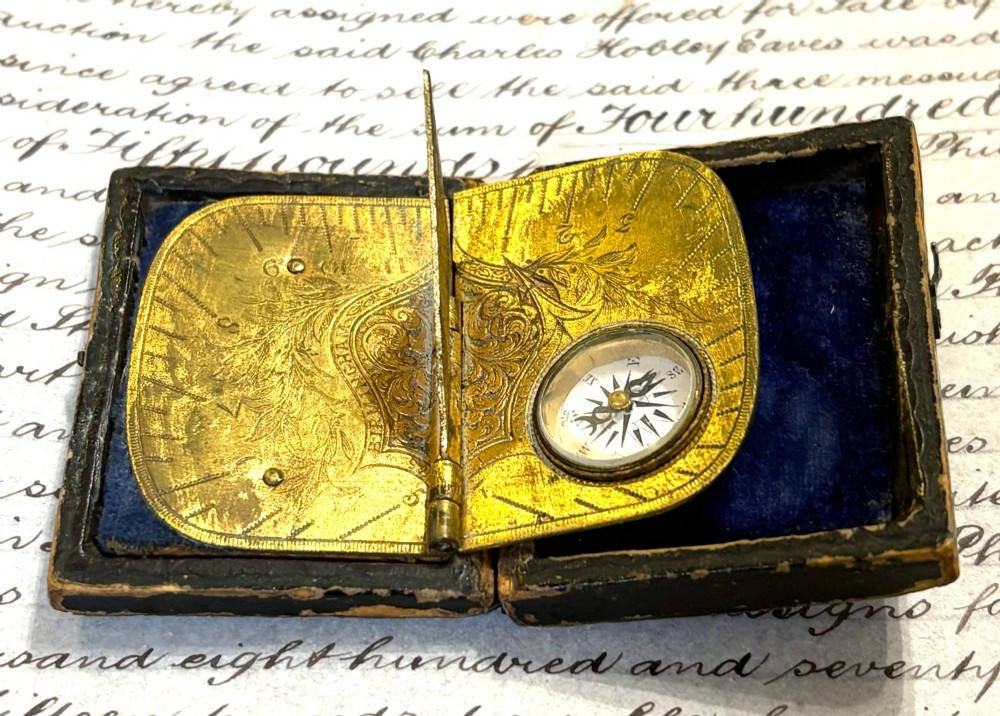 An engraved Victorian brass folding pocket sundial with an integrated compass inside a velvet-lined case. View II