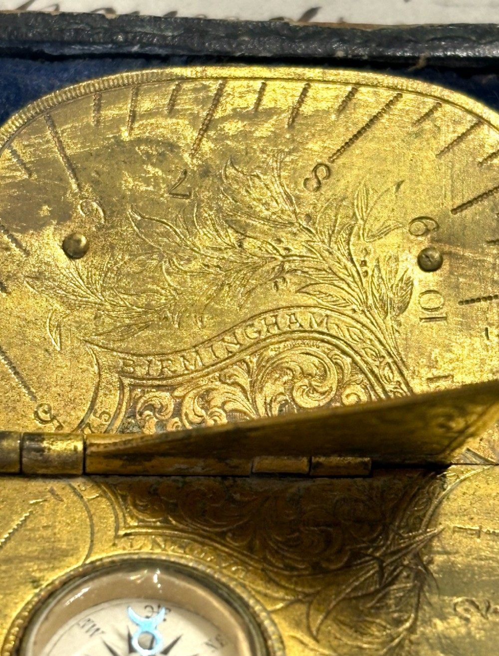 An engraved Victorian brass folding pocket sundial with an integrated compass inside a velvet-lined case. View V