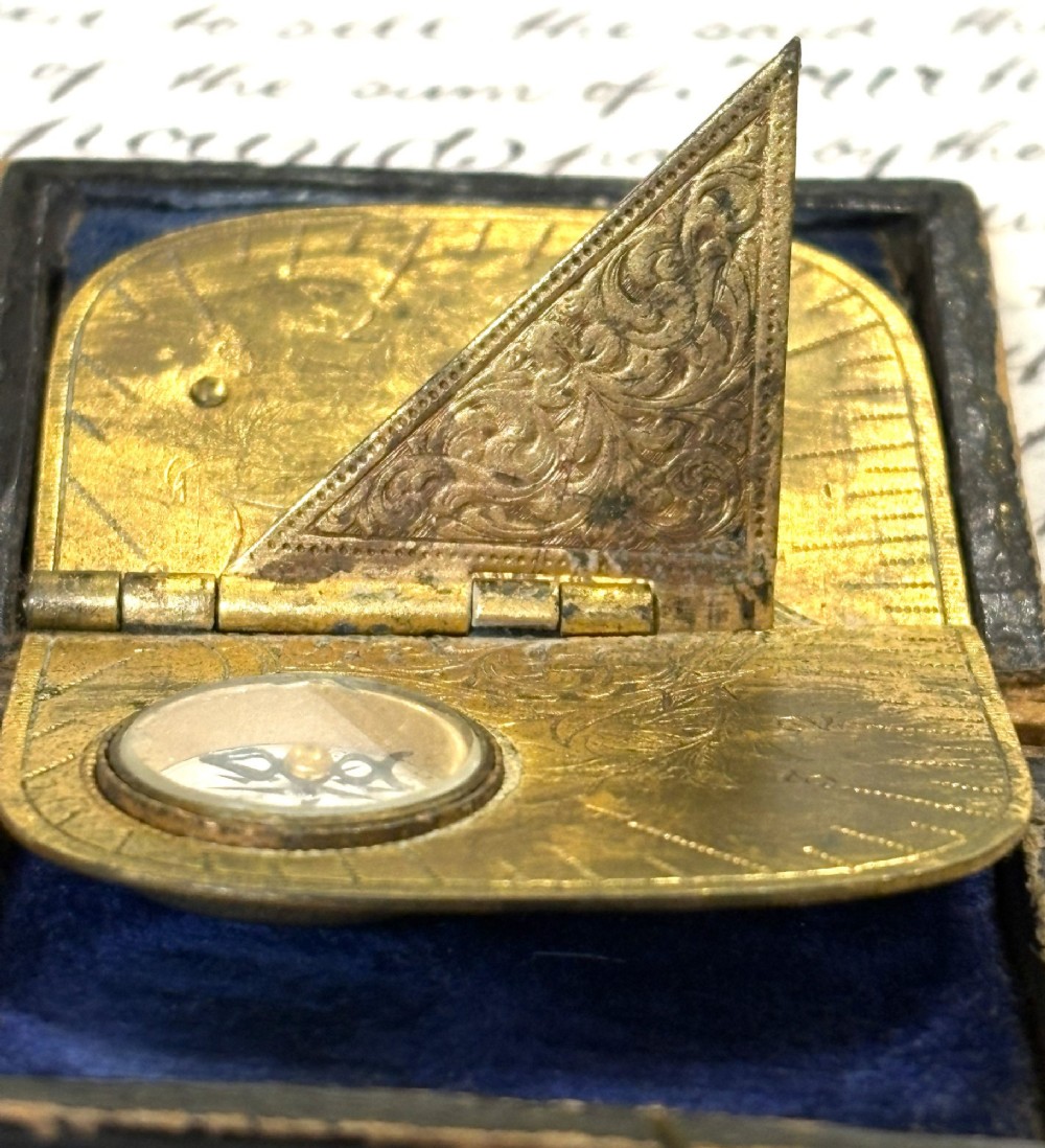 An engraved Victorian brass folding pocket sundial with an integrated compass inside a velvet-lined case. View VI