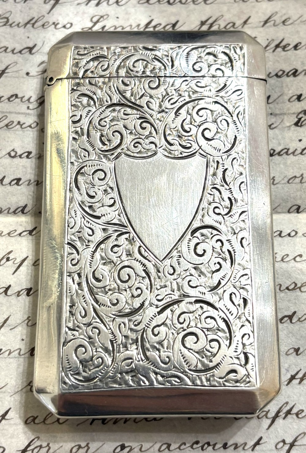 A rectangular Victorian sterling silver card case featuring intricate scroll engraving and an unengraved central heart-shaped shield.