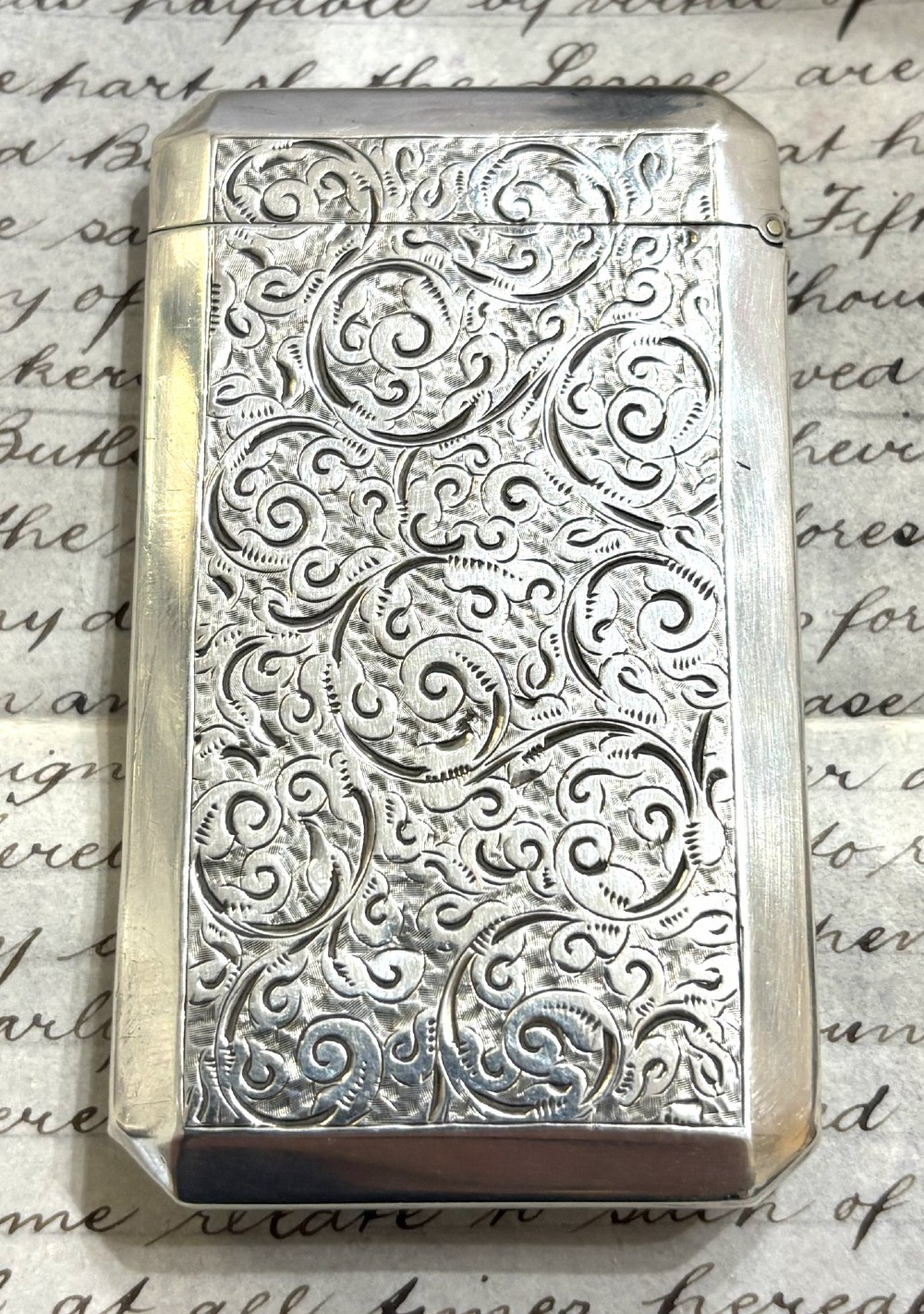 A rectangular Victorian sterling silver card case featuring intricate scroll engraving and an unengraved central heart-shaped shield. View II
