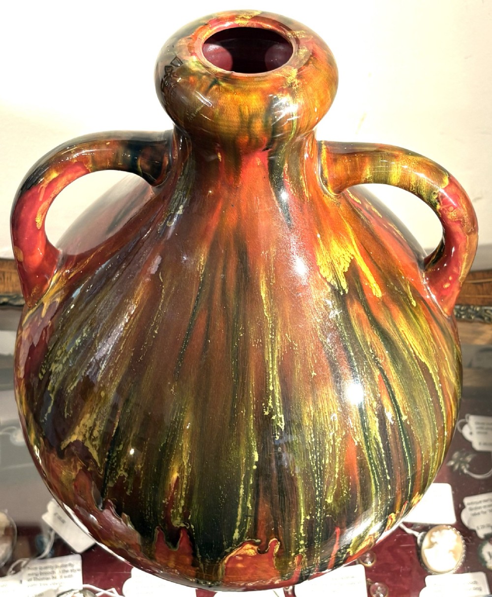 A bulbous ceramic vase featuring twin loop handles and a glossy multi-coloured running glaze in shades of red, green, and dark brown. View II