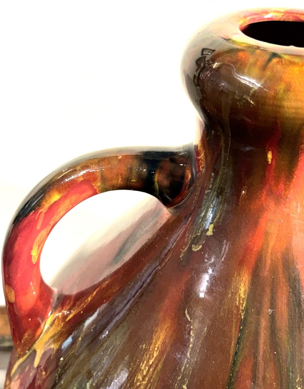 A bulbous ceramic vase featuring twin loop handles and a glossy multi-coloured running glaze in shades of red, green, and dark brown. View III