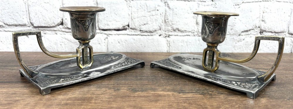 A pair of antique Art Nouveau WMF chambersticks crafted from aged silver-coloured metal with brass geometric handles and relief bases.