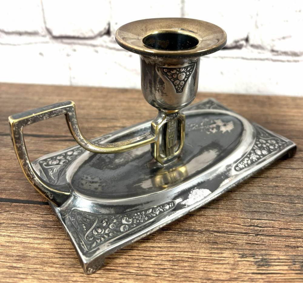 A pair of antique Art Nouveau WMF chambersticks crafted from aged silver-coloured metal with brass geometric handles and relief bases. View II