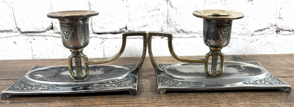A pair of antique Art Nouveau WMF chambersticks crafted from aged silver-coloured metal with brass geometric handles and relief bases. View IV