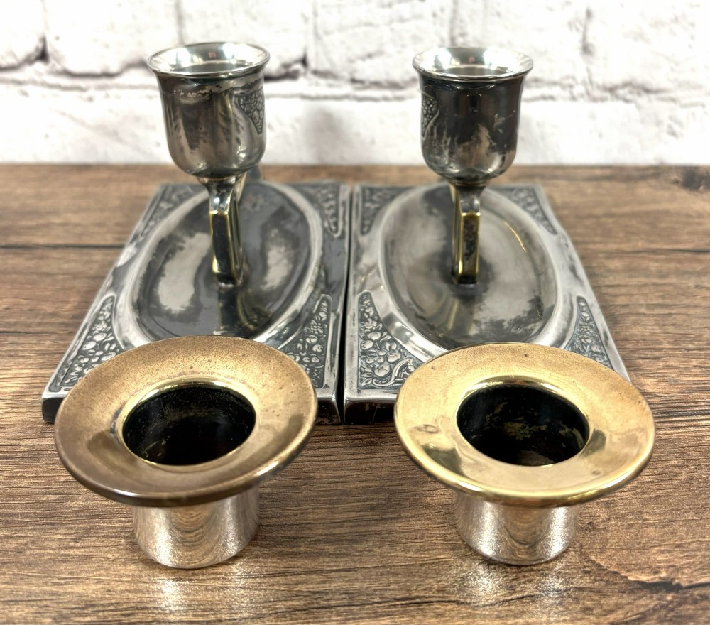 A pair of antique Art Nouveau WMF chambersticks crafted from aged silver-coloured metal with brass geometric handles and relief bases. View V