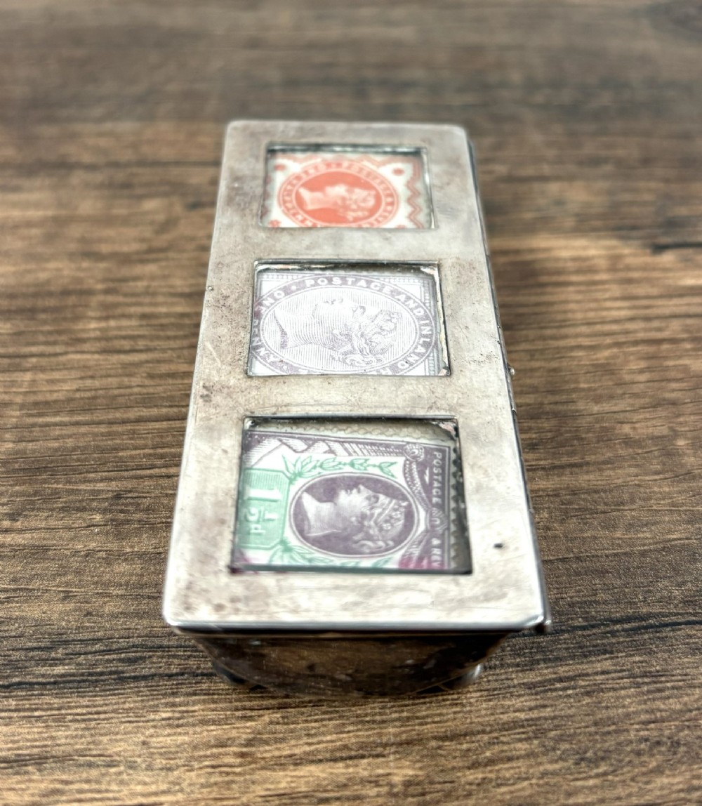A rectangular silver triple stamp holder with three glazed glass display panels resting on four small spherical ball feet. View II